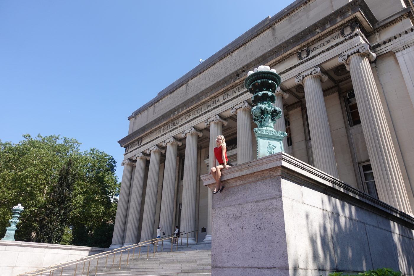 Madeline in a red top sitting on the stone ledge outside Columbia's library