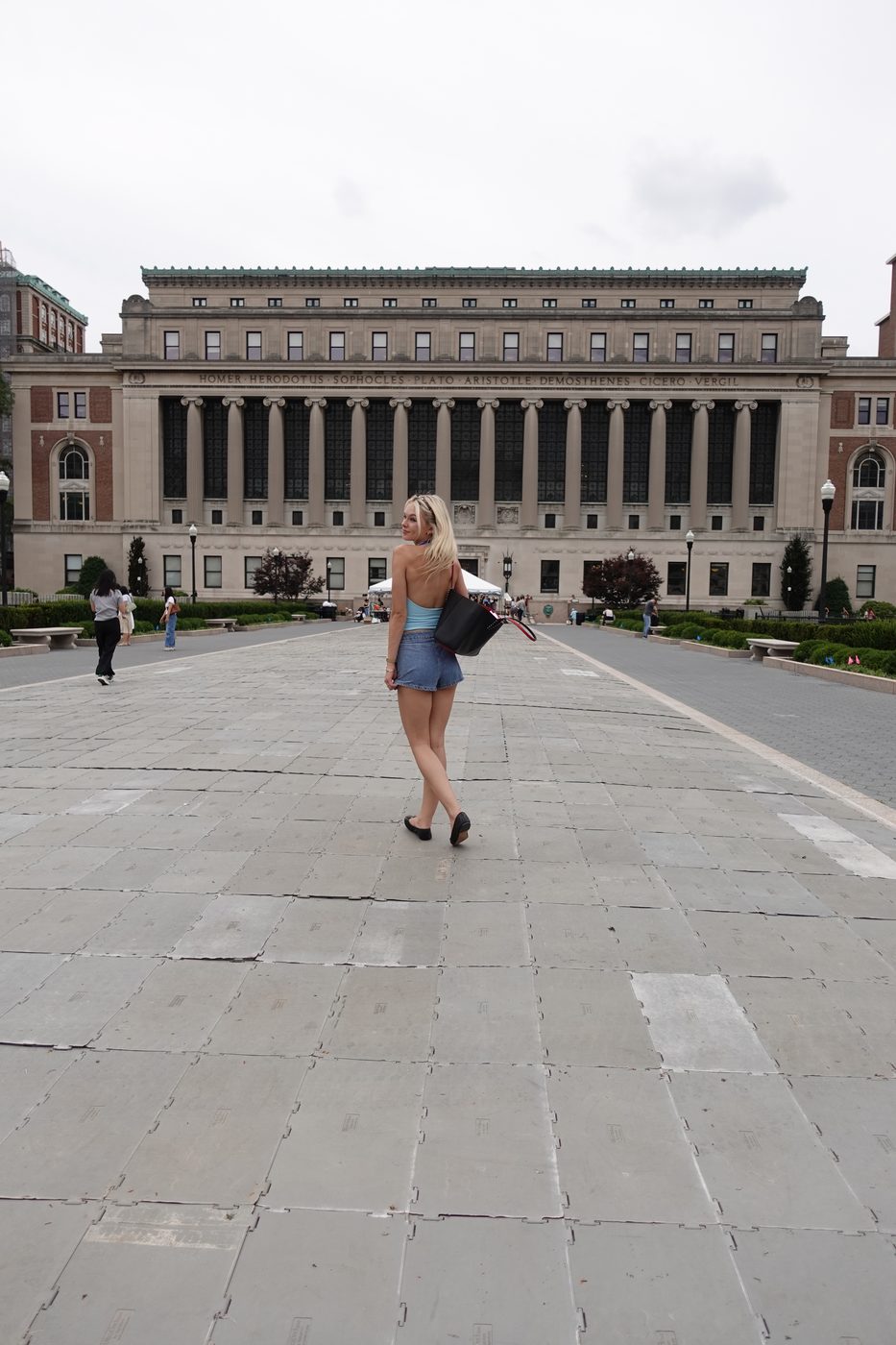 Madeline walking across Columbia's campus in a blue halter and denim shorts, looking back