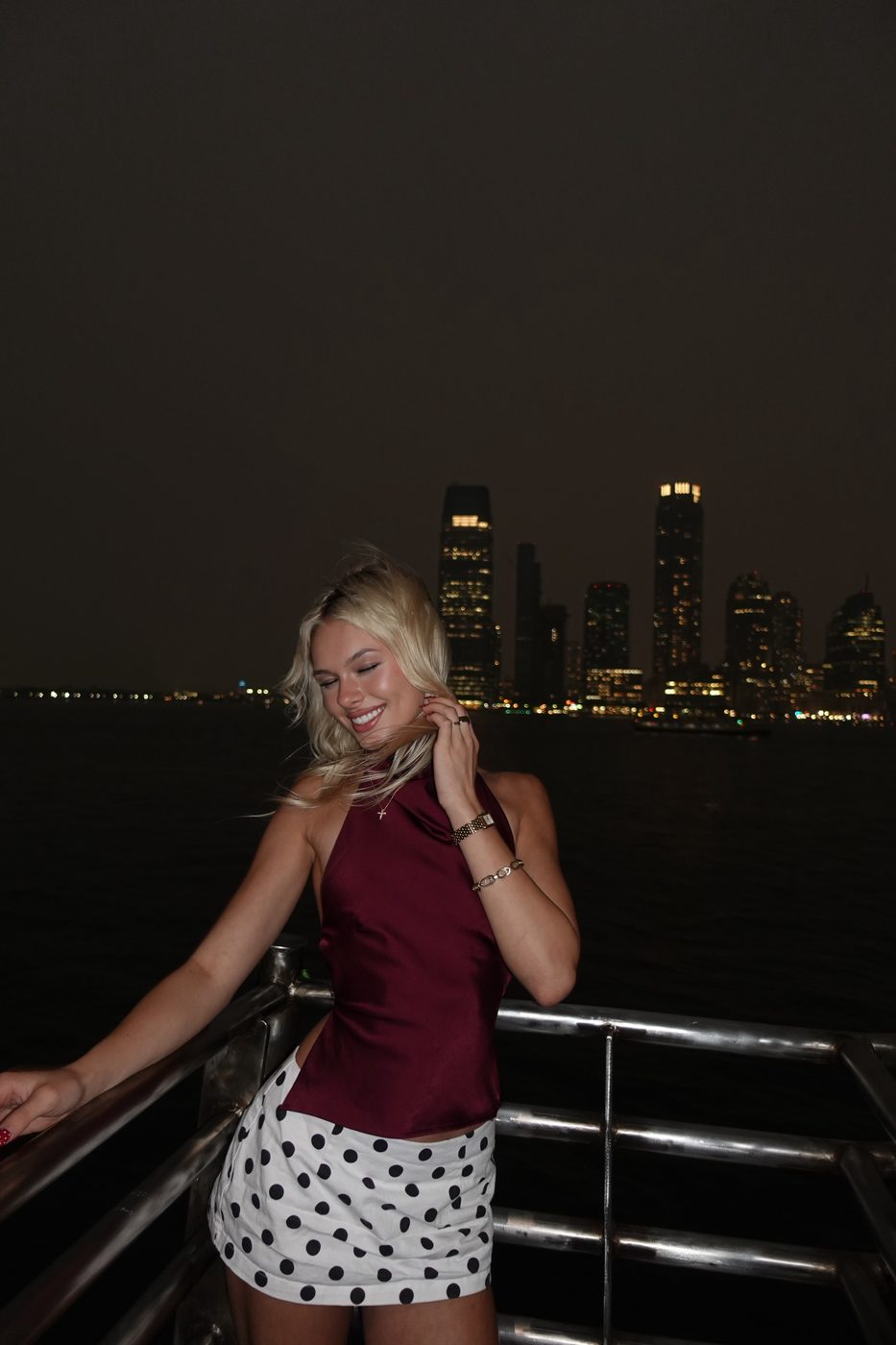 Madeline by the water at night with the city skyline behind her