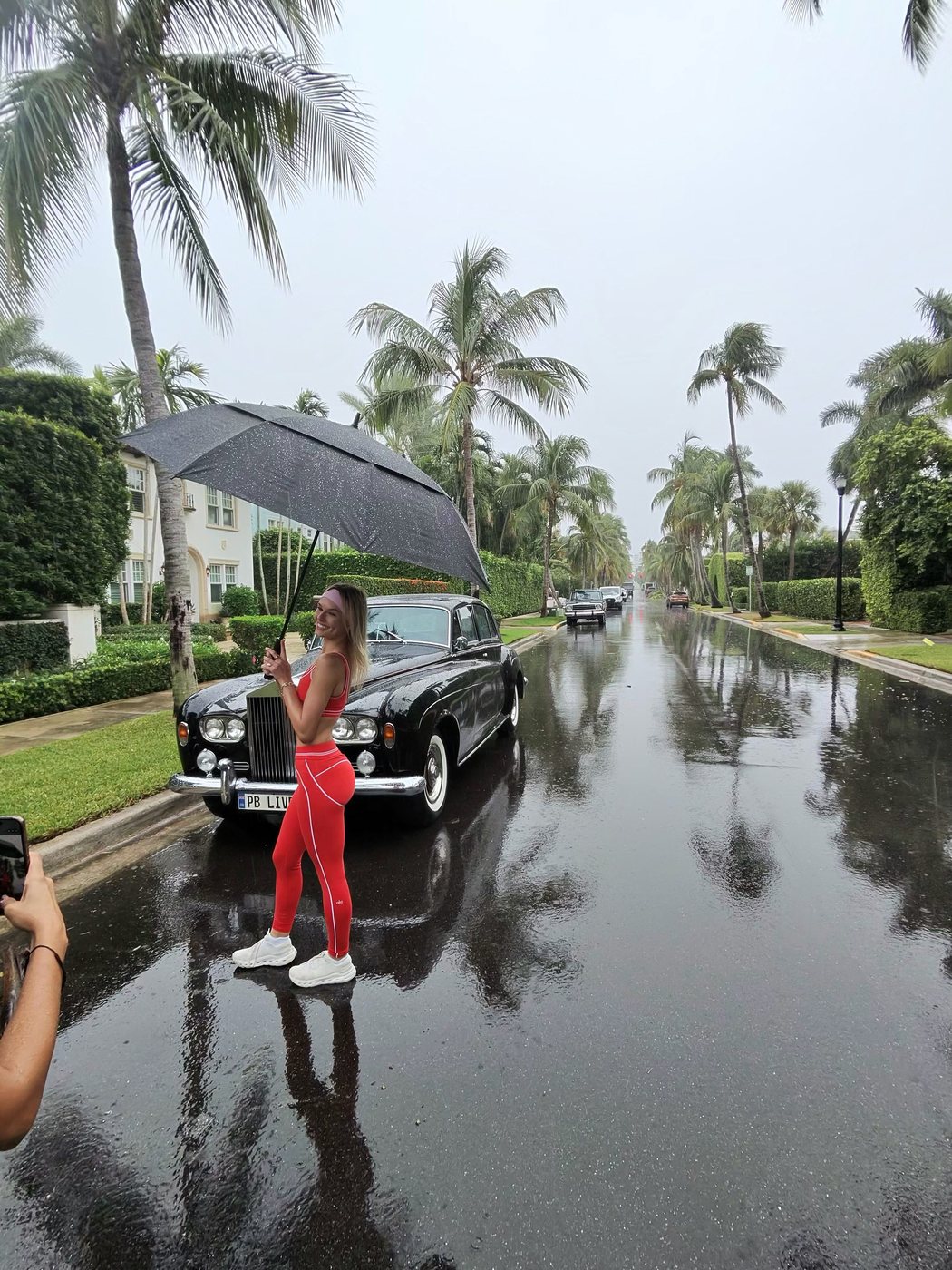 Madeline in red on a wet palm lined street beside a vintage car